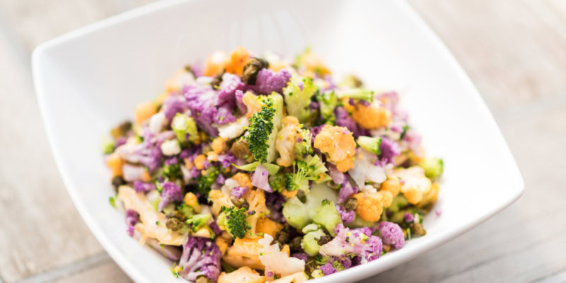 A colorful Brassica salad featuring purple cabbage, broccoli, and carrots, served in a white bowl for a fresh, healthy meal.