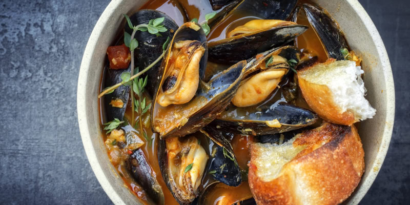 Seafood cioppino with mussels, bread, and herbs in a rustic bowl.