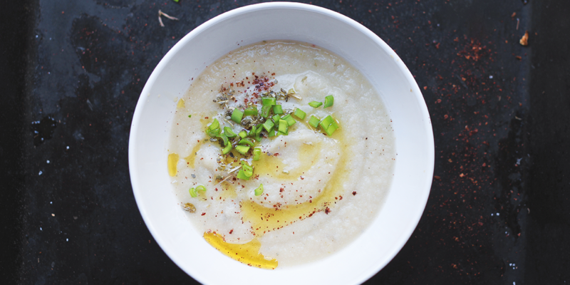 A bowl of creamy cauliflower soup garnished with chopped green onions and a drizzle of olive oil.