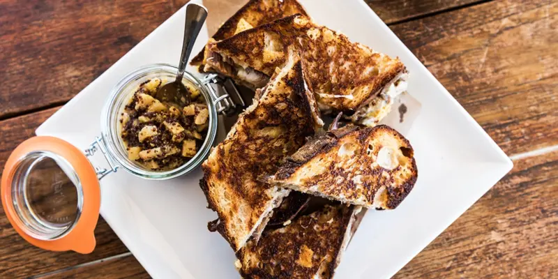 Delicious duck confit grilled cheese with pear mostarda on a white plate.