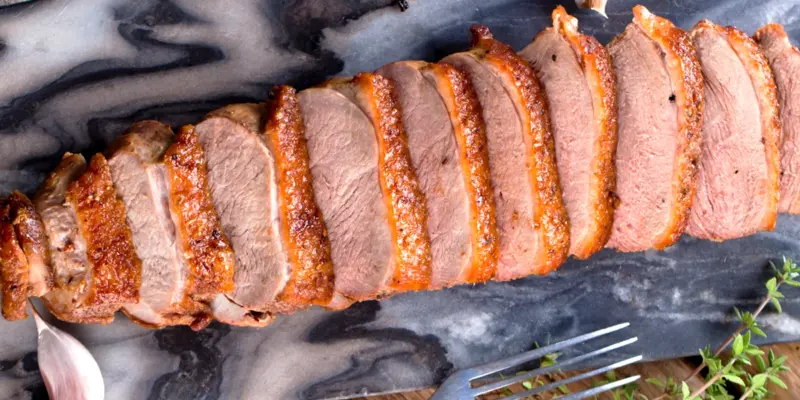 Crispy duck breast sliced with golden skin, served on a dark marble surface with fresh herbs.