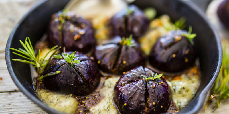 Balsamic figs with feta cheese and herbs in a black dish, showcasing a savory spread.