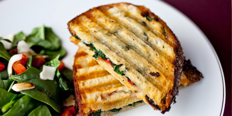 Grilled panini with roasted red peppers, melted Fontina cheese, and fresh greens on a white plate.