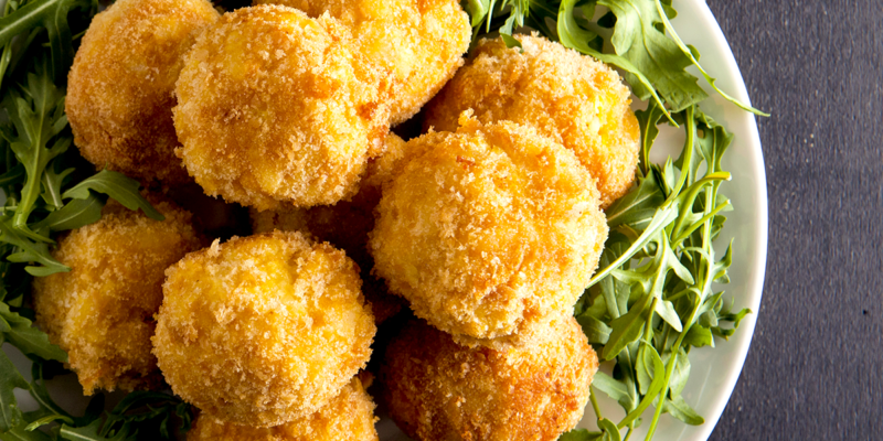 Crispy fried green olives stuffed with flavorful filling, served with fresh greens on a white plate.