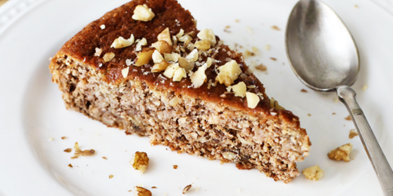 Slice of Greek Walnut Cake with chopped walnuts on top, served on a white plate with a spoon.