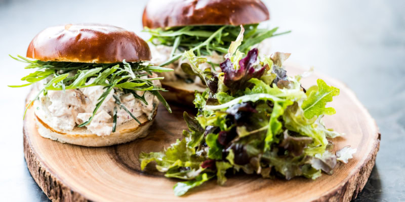 Delicious chicken salad sandwich with fresh greens on a brioche bun, served with a side of mixed greens.