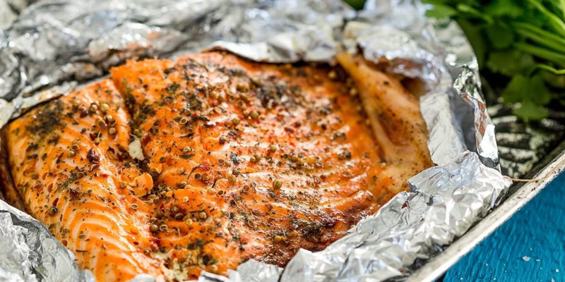 Grilled wild salmon fillet seasoned with herbs and spices, cooked in foil on a grill.