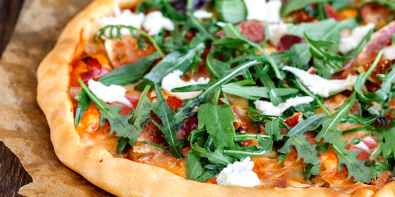 Close-up of a tart topped with heirloom tomatoes, baby mozzarella, and arugula, served on a rustic wooden surface.