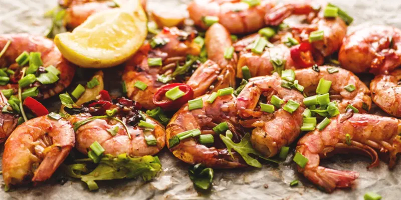 Close-up of spicy grilled shrimp garnished with green onions and lemon wedge, served on a plate.
