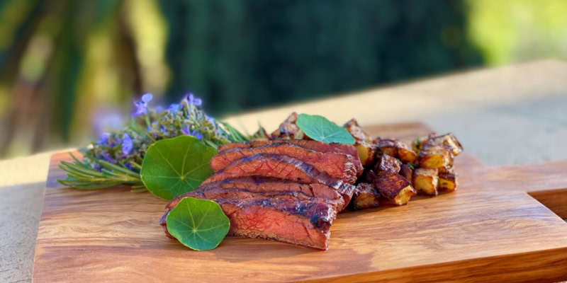 Miso marinated steak grilled to perfection, served with fresh herbs and roasted vegetables on a wooden cutting board.