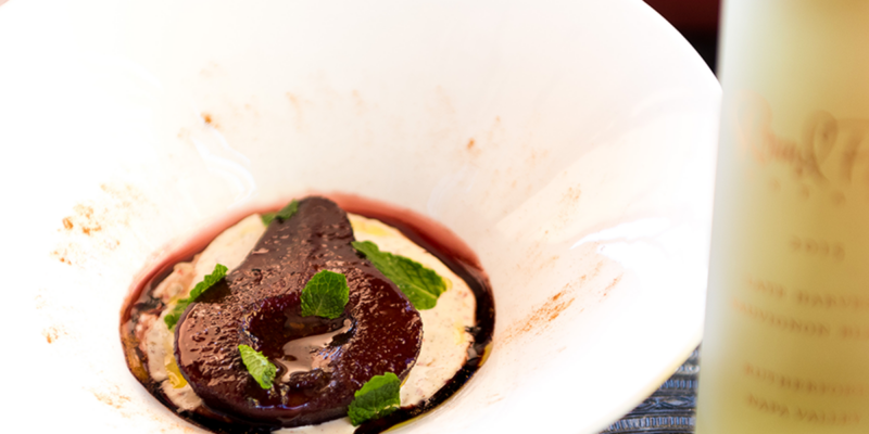 Poached pear served with pink pepper-infused mascarpone cheese, garnished with fresh mint leaves, on a white plate.