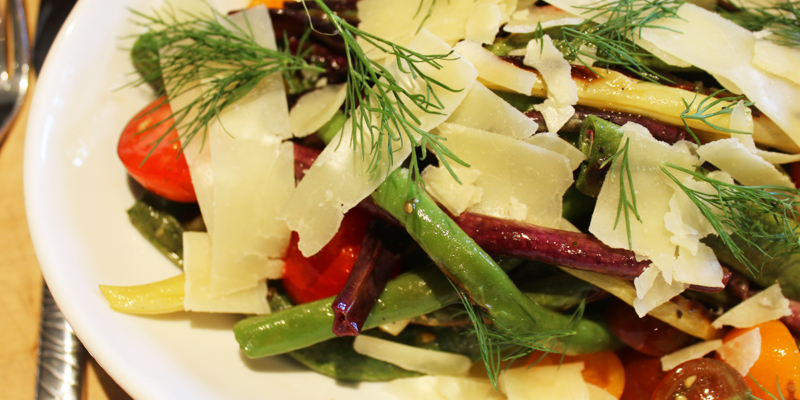 Bright, fresh pole bean salad with charred beans, cherry tomatoes, and shaved cheese garnished with dill.