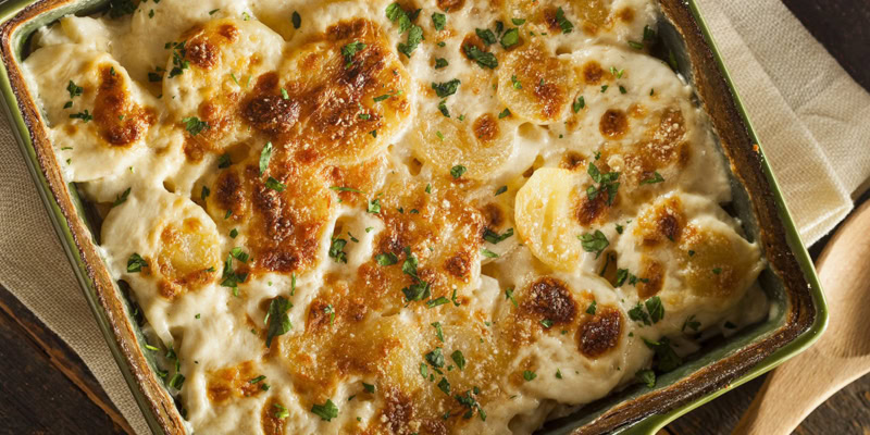 Baked cauliflower and potato gratin with golden cheese crust and fresh herbs in a baking dish.