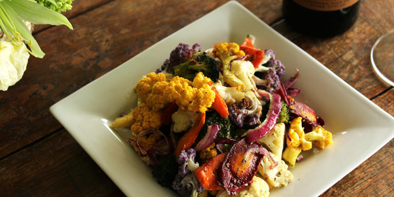 Colorful roasted vegetable medley on a white square plate, featuring cauliflower, red peppers, purple cabbage, and broccoli.