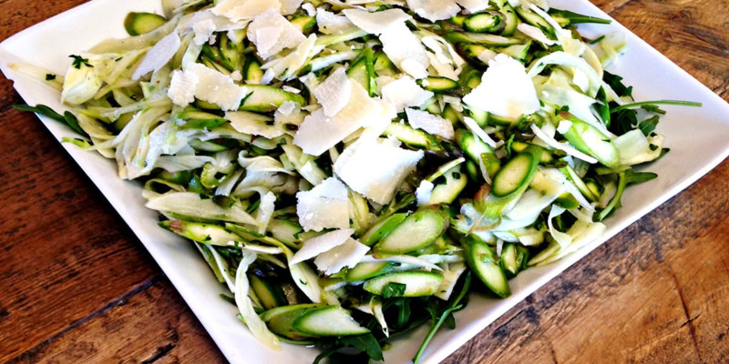 Close-up of shaved asparagus and fennel salad on a white plate, garnished with cheese shavings.