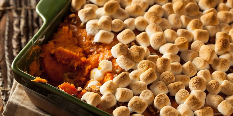Baked sweet potatoes topped with toasted marshmallows and a hint of Fernet flavor, served in a green baking dish.