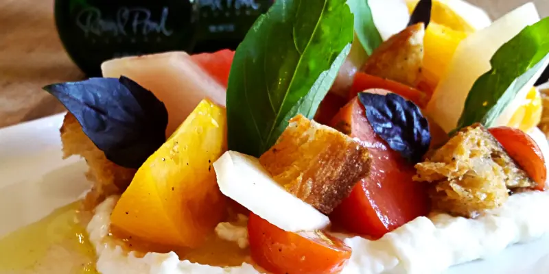 Fresh heirloom tomatoes with creamy burrata cheese, basil leaves, and croutons on a white plate.