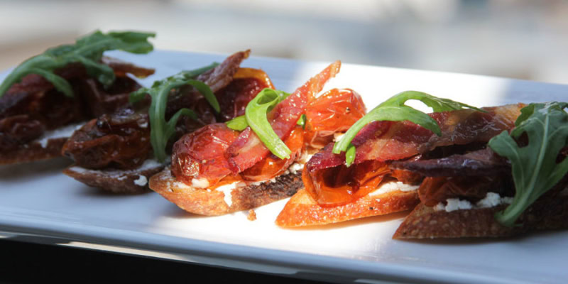 Close-up of B.L.T. crostini with bacon, tomato, and arugula on toasted bread.