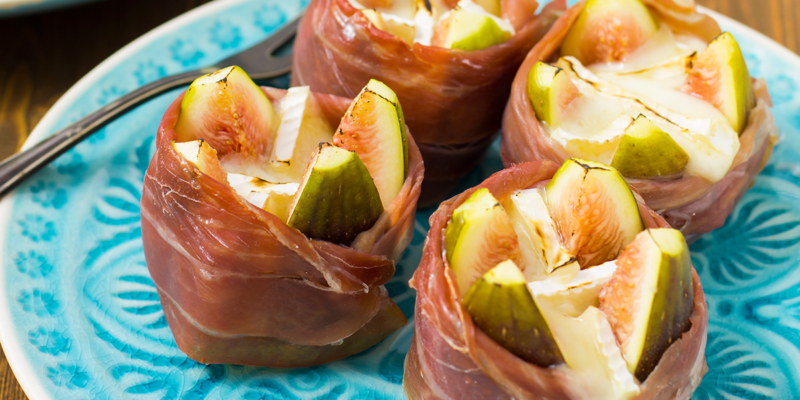 Delicious figs filled with creamy goat cheese, wrapped in prosciutto, served on a decorative blue plate.