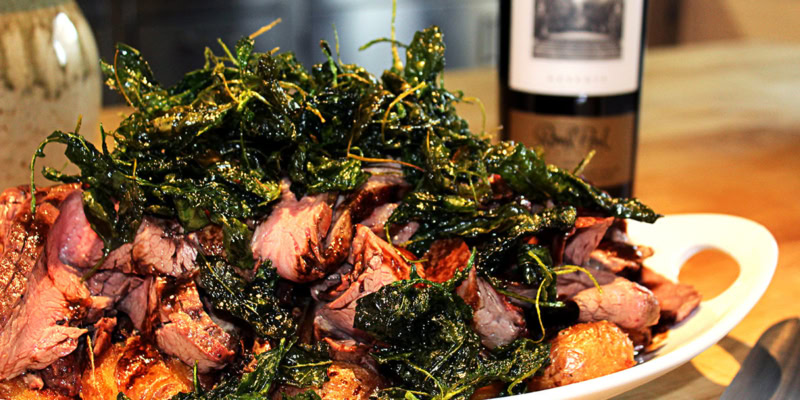 Delicious grilled flank steak with crispy potatoes and fresh herbs on a wooden table.