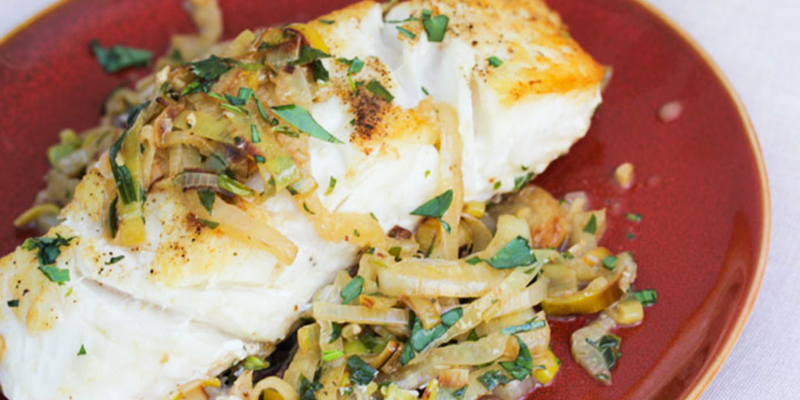 Freshly cooked halibut fillet topped with sautéed leek and fennel, served on a red plate.