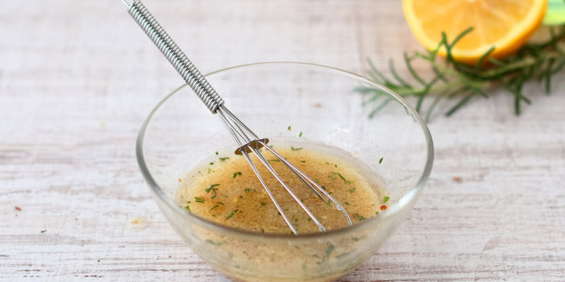 Fresh Meyer Lemon Vinaigrette in a glass bowl with a whisk, garnished with lemon slices and herbs.