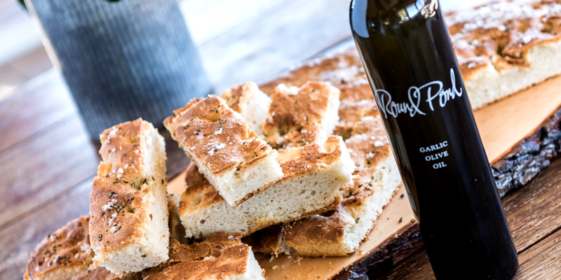 Herbed focaccia bread topped with herbs, served alongside a bottle of garlic olive oil on a rustic wooden table.