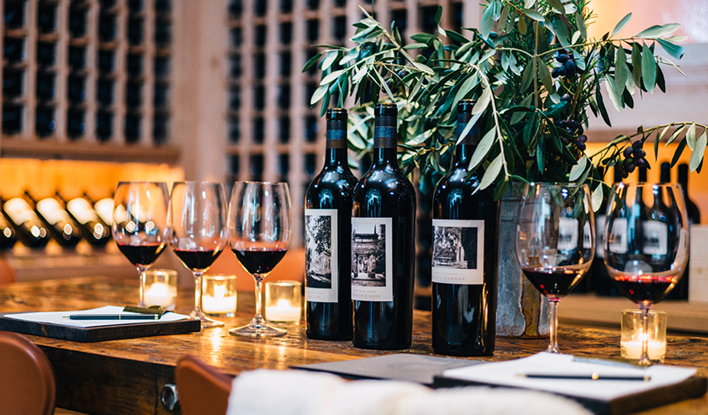 Wine bottles and glasses set on a wooden table with a lush plant, perfect for private and large group experiences.