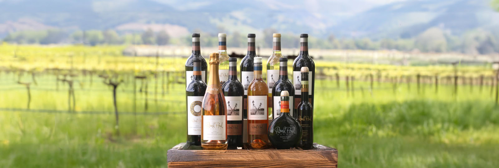 Bottles of premium wine from Round Pond Estate displayed outdoors with vineyard in background.